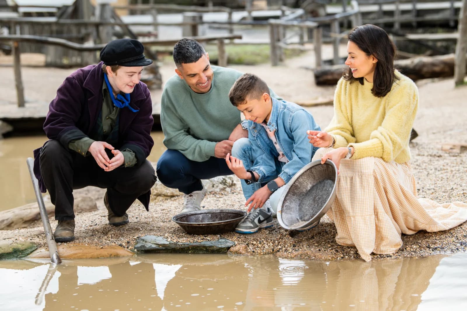 A family of four engaging in gold panning by a muddy pool of water