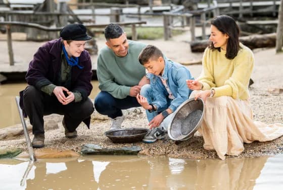 A family of four engaging in gold panning by a muddy pool of water