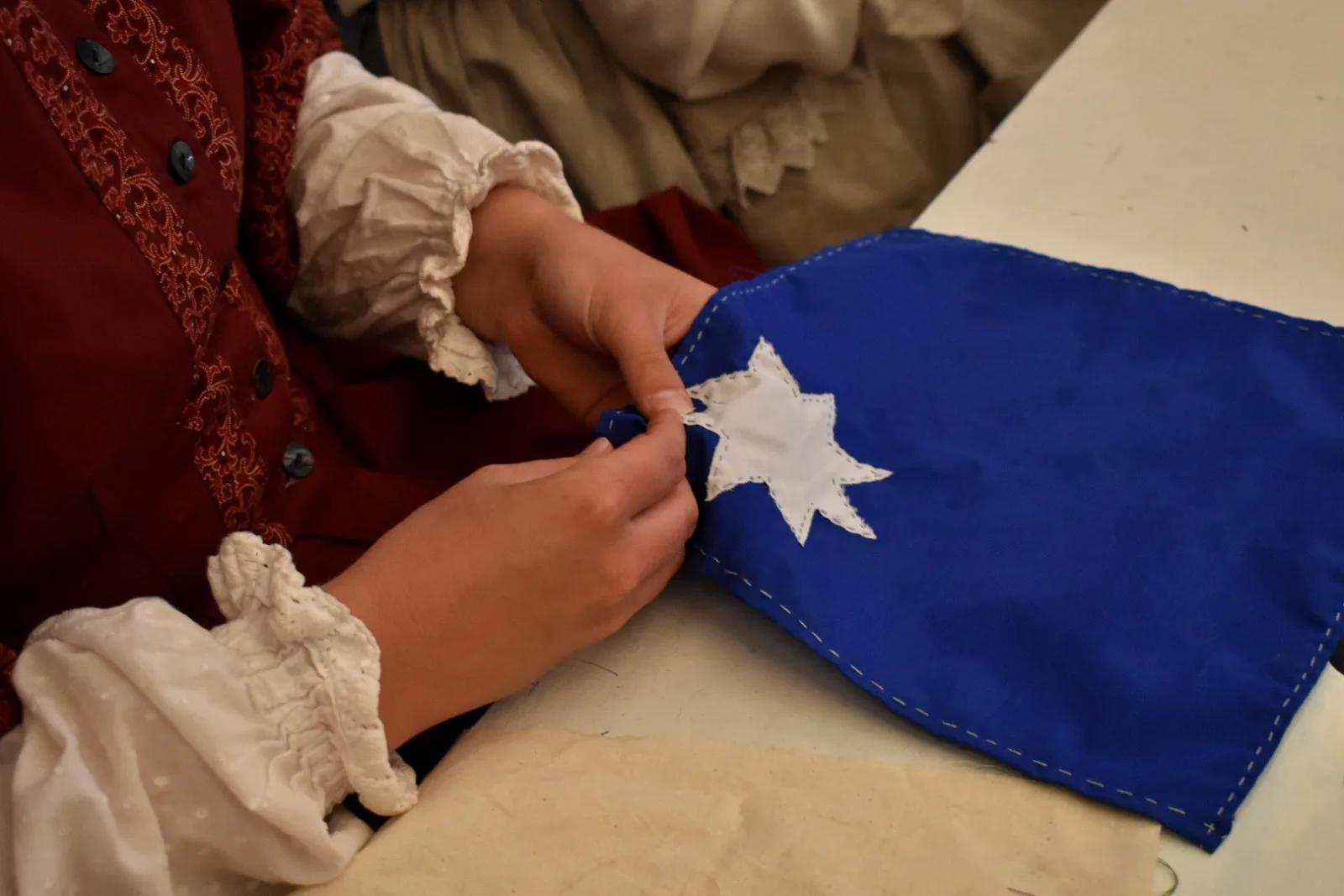 A person's hands sewing a white star onto a blue fabric flag. The flag resembles the Eureka Flag, a symbol of the 1854 Eureka Stockade rebellion in Australia.