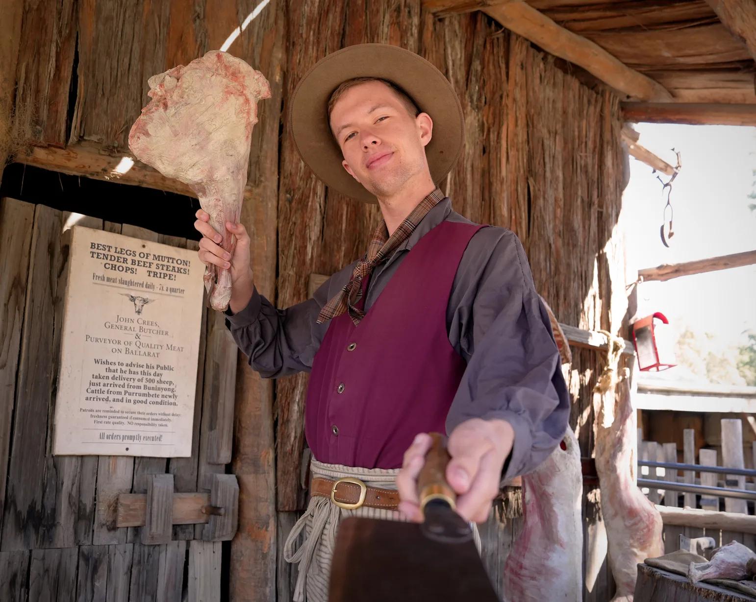 Goldfields butcher reenactor holding fresh meat outside a rustic wooden shop, from Australia’s most visited outdoor museum and heritage attraction.