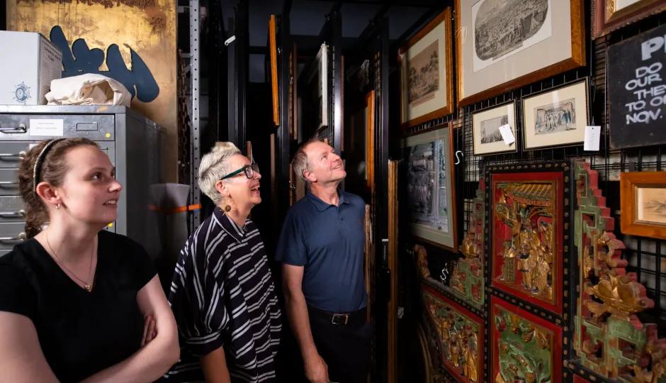 Behind-the-scenes tour of a museum's art collection at Sovereign Hill, with participants looking at various framed pieces stored on movable racks, including historical prints and intricate carvings.