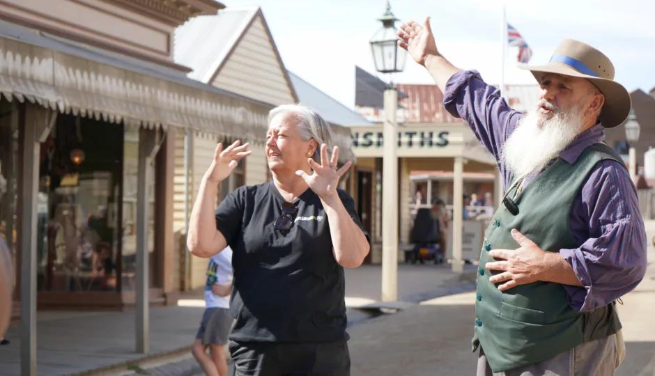 Two men engage in lively conversation on the historic streets of Sovereign Hill, one gesturing animatedly while the other listens with hands raised, capturing the spirited atmosphere and gold rush-era charm of Sovereign Hill’s living history experience.
