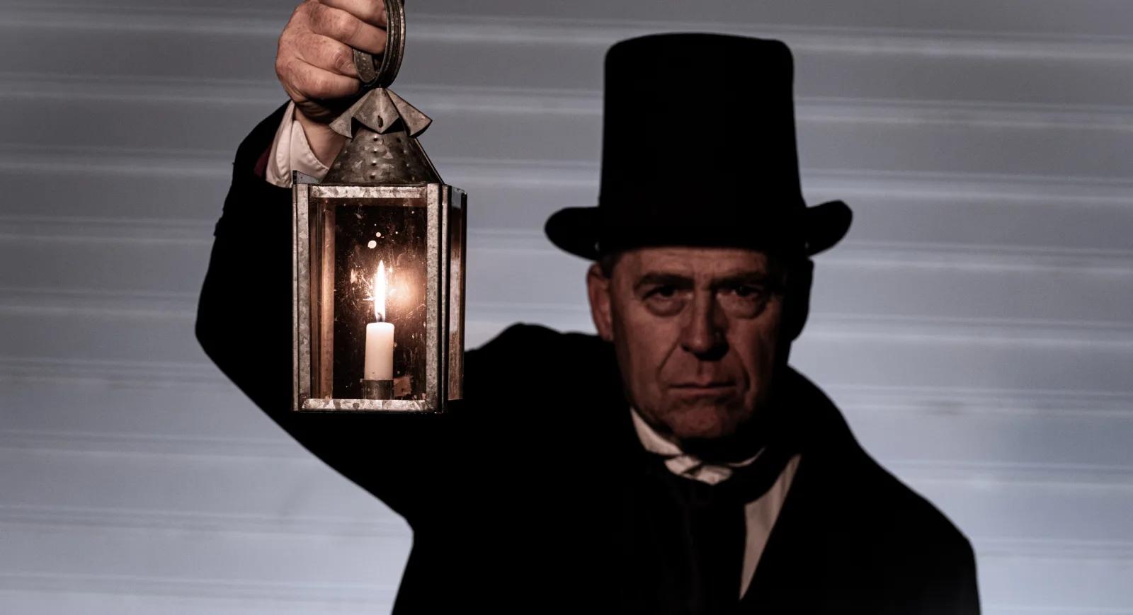 Costumed man in a top hat holding a candle lantern during a spooky Halloween tour experience at Sovereign Hill.