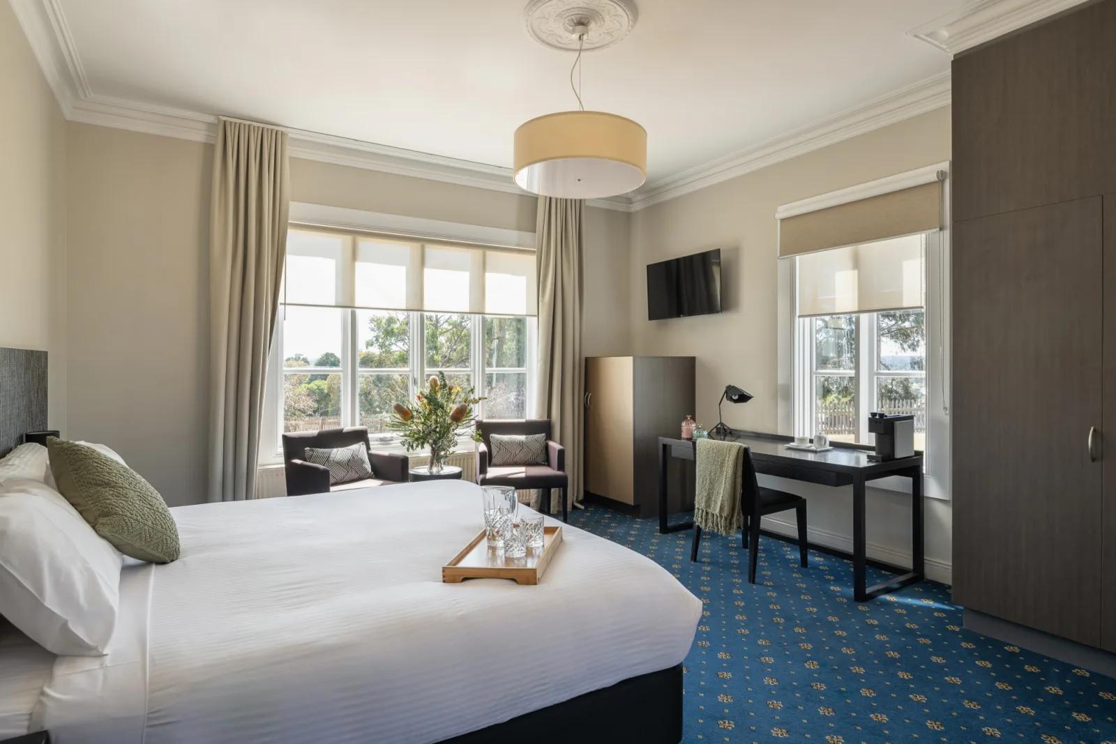 A room at Sovereign Hill Hotel offering a comfortable bed, sitting area, and work desk with ample natural light.
