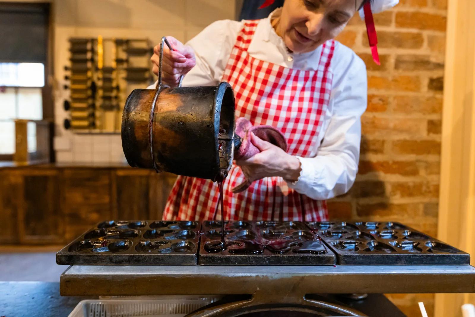 A baker pouring batter into molds to make small cakes or pastries.