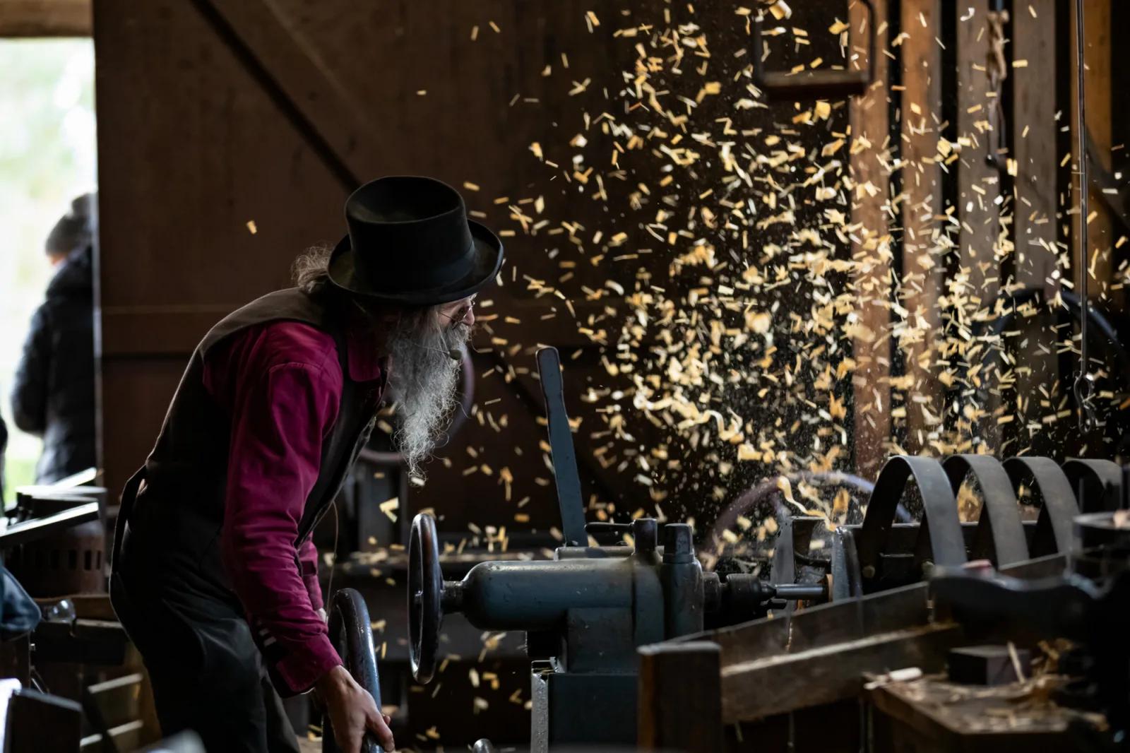 A man working with wood in a workshop, using tools and machinery to create wooden objects.
