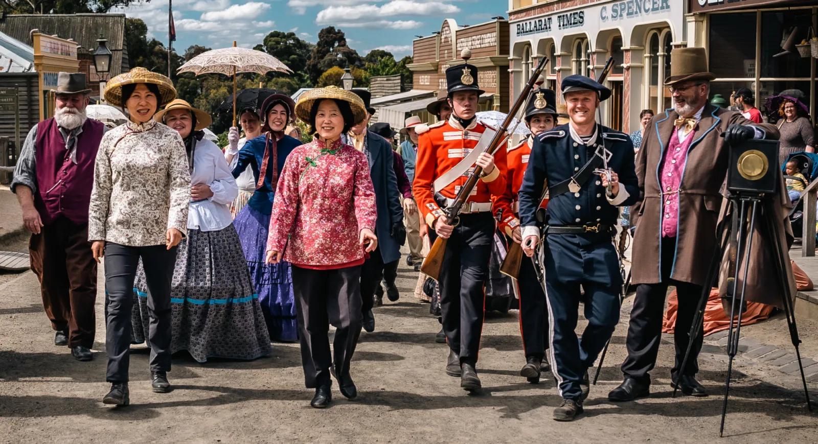 Multicultural parade with costumed diggers, soldiers, and community members marching down heritage street, from Australia’s most visited outdoor museum and heritage attraction.