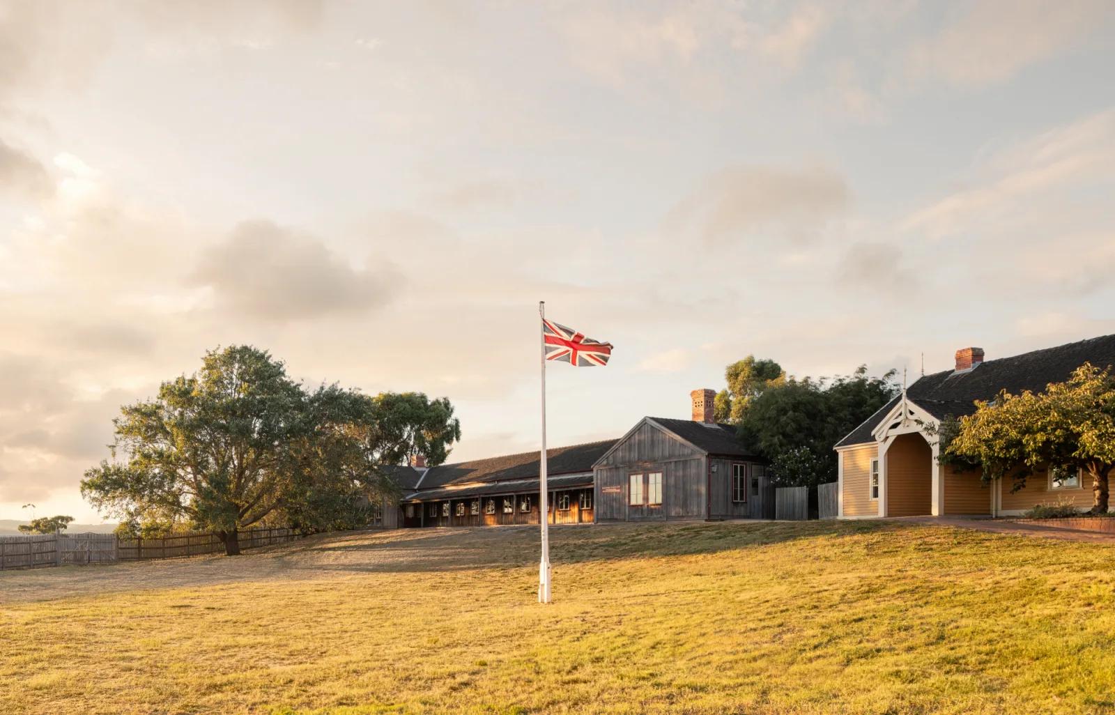 Union Jack flag flying outside heritage homestead buildings at sunset, from Australia’s most visited outdoor museum and heritage attraction.