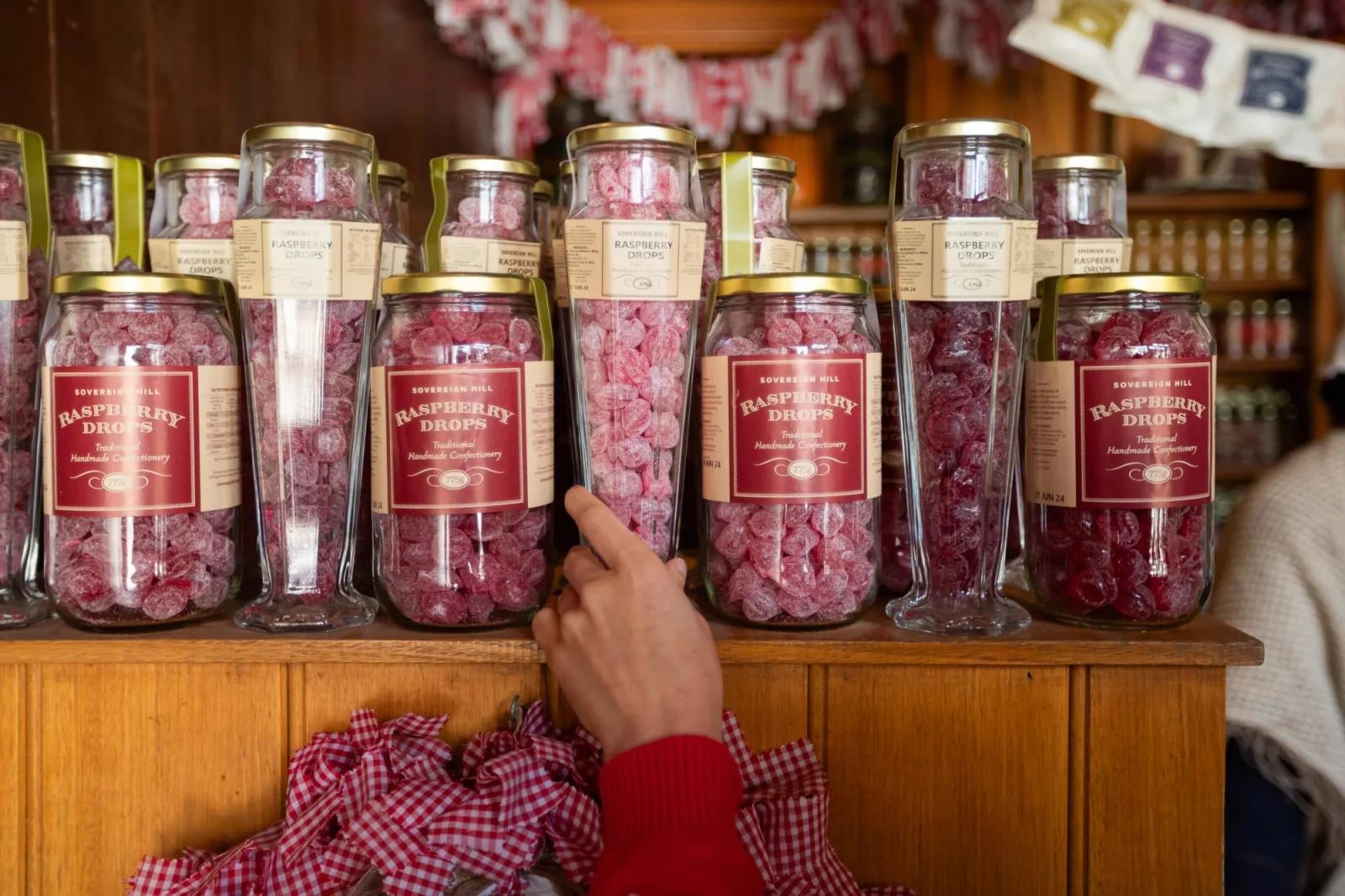 Jars of traditional handmade raspberry drops displayed on a wooden counter inside Sovereign Hill’s confectionery store.