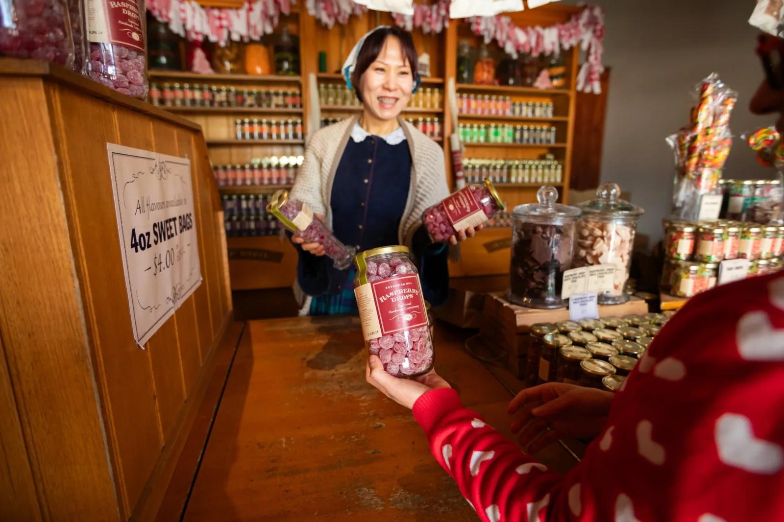 Costumed shopkeeper serving a jar of raspberry drops to a customer inside C. Spencer’s traditional confectionery at Sovereign Hill.