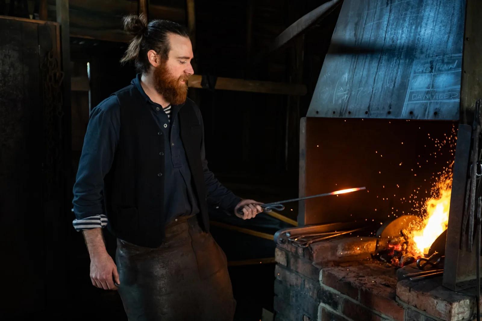 Blacksmith heating a metal rod in a blazing forge inside the traditional workshop at Sovereign Hill.