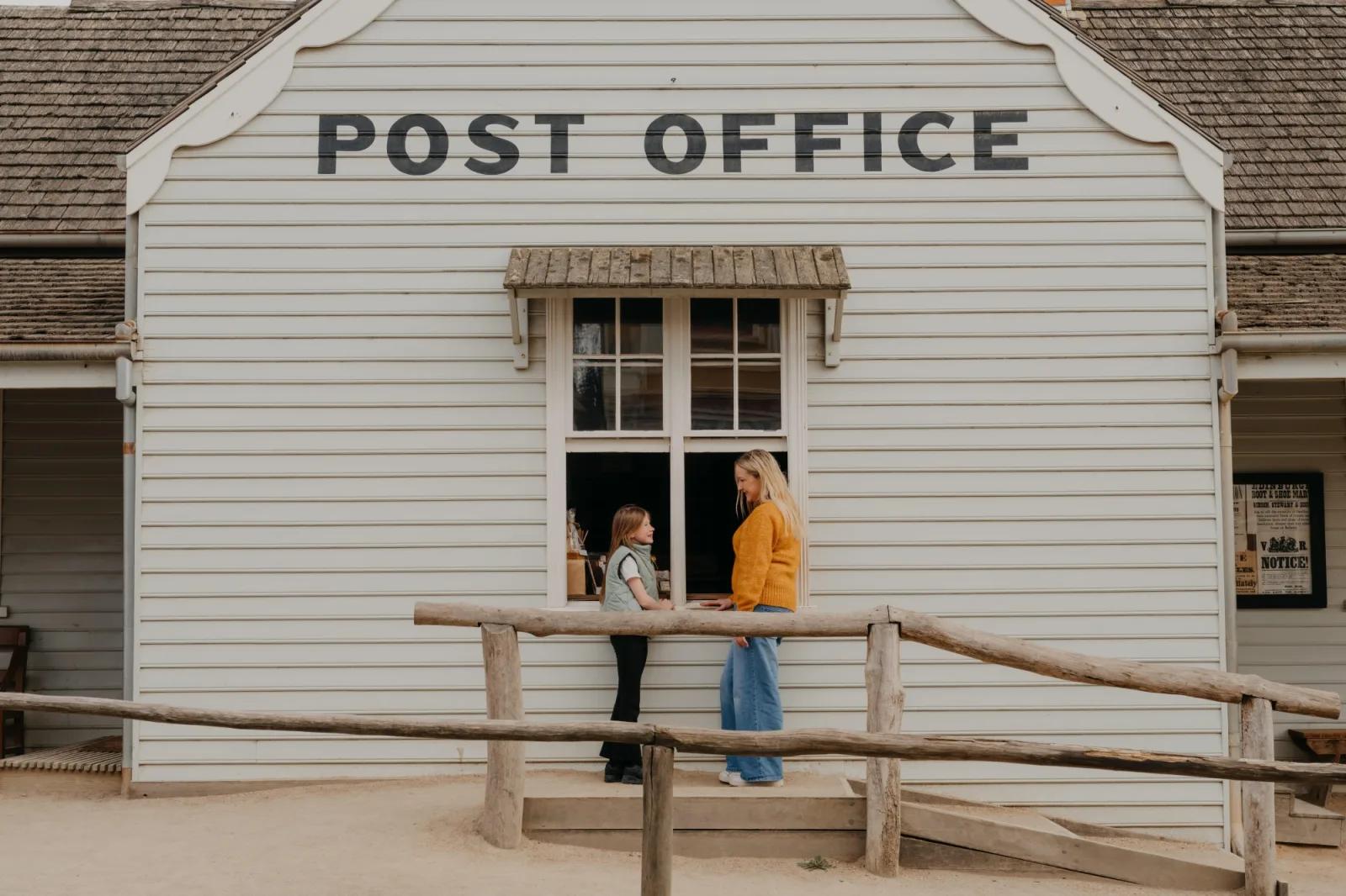 Woman and child visiting the historic Post Office counter at Sovereign Hill, with a timber accessibility ramp in front.