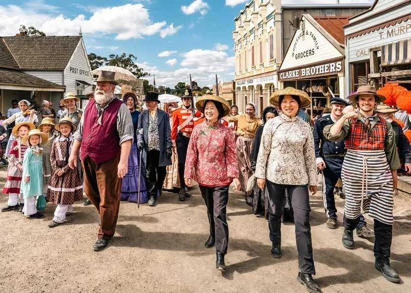 Costumed goldfields migrants gathered around a wooden cart and luggage, representing Gold Rush immigration at Sovereign Hill.