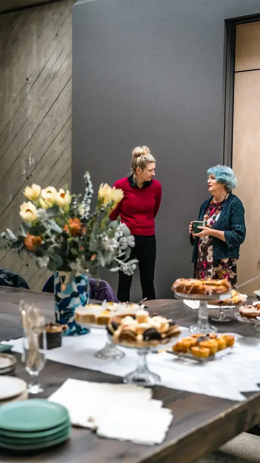 Two women talking beside a table of flowers, pastries and refreshments at Sovereign Hill’s Rare Trades Centre.