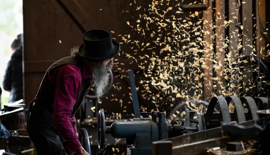 A man working with wood in a workshop, using tools and machinery to create wooden objects.