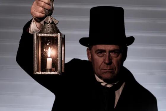 Costumed man in a top hat holding a candle lantern during a spooky Halloween tour experience at Sovereign Hill.